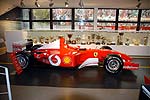 Formel 1 Wagen der Saison 2001, dahinter Pokale aus alle möglichen Jahren und Rennen